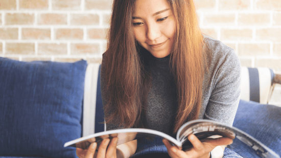 asian woman reading a magazine on a couch