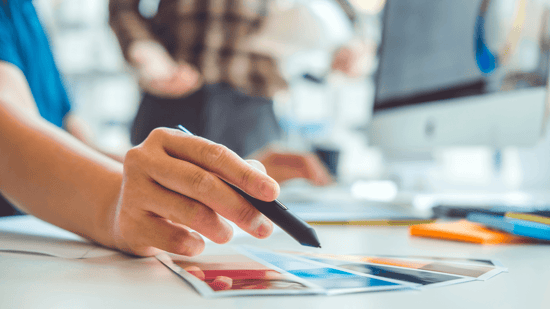 A zoomed-in photo that emphasizes a hand holding a smart pen and comparing various colors on a computer desk