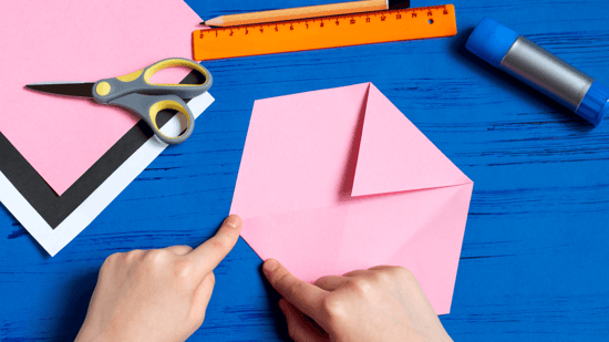 person folding a pieces of paper into a hexagon, with a ruler and scissors and pencil above it